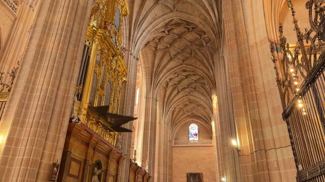 Slow tilt up shot capturing the ornate golden pipe organ and intricate vaulted ceiling inside the historic Segovia Cathedral in Segovia, Spain.