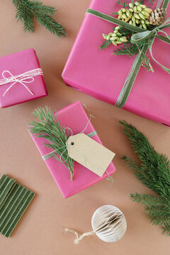 Overhead view of wrapped Christmas gifts decorated with blank gift tags, evergreen sprigs, velvet ribbon, pinecones, Christmas baubles and ornaments on a beige background