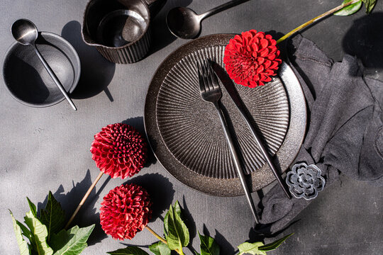 Close-up overhead view of a rustic place setting decorated with dark red Pompon Dahlias on a grey concrete table