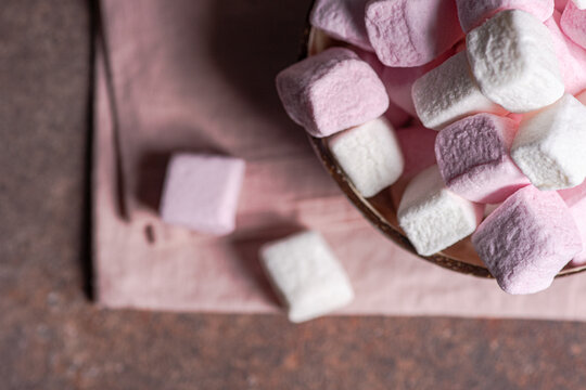 Overhead view of a bowl of pink and white marshmallows on a napkin and concrete table