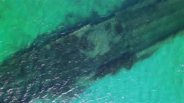 Aerial 4K pull-away shot of the historic Milo shipwreck visible through clear turquoise sea.
