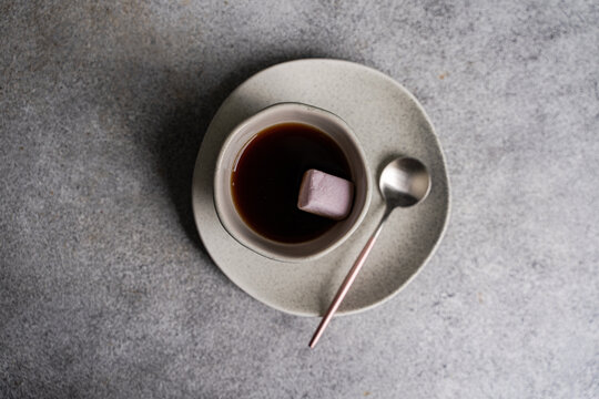 Close-up overhead view of a cup of black coffee with a pink marshmallow  on a grey concrete table