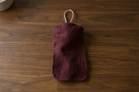 Handcrafted merino fleece windsock on walnut studio floor with burgundy tones