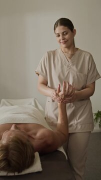 Vertical shot of young adult Caucasian masseuse massaging arm and wrist of Caucasian male client. Video ideal for rehabilitation center commercials or physical therapy promos