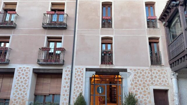 Straight-on shot of a historic building with intricate geometric sgraffito facade, traditional iron balconies, and a warm tourist information entrance in Segovia, Spain.