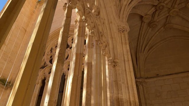 Panning shot exploring the intricate limestone columns and ornate gothic vaulting softly lit by natural morning sun inside the Segovia Cathedral in Segovia, Spain.
