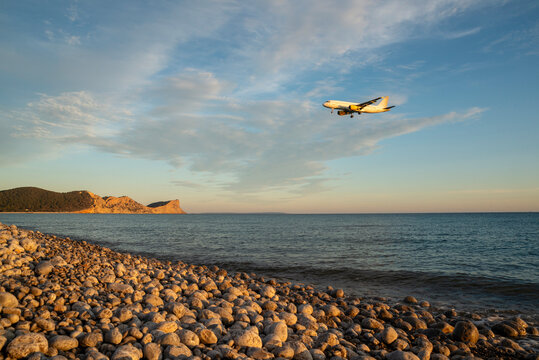 Close-up side view of a low flying Aircraft over a rocky beach at sunset, Ses Salines Natural Park, Ibiza, Balearic Islands, Spain