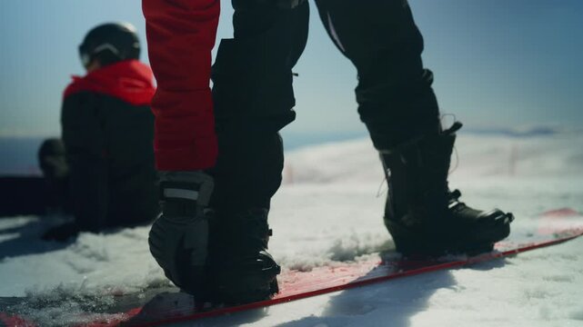 A snowboarder fastens their binding, ready to descend a pristine slope. Two friends enjoy winter sports together in a stunning snowy landscape.