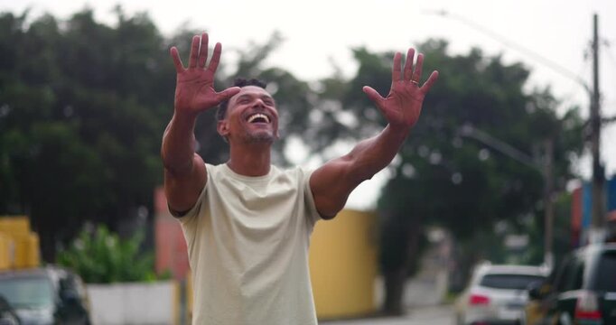 Man of African descent raising hands in gratitude and prayer, smiling upward in hope and faith, a serene moment of devotion and connection to God in an urban outdoor setting