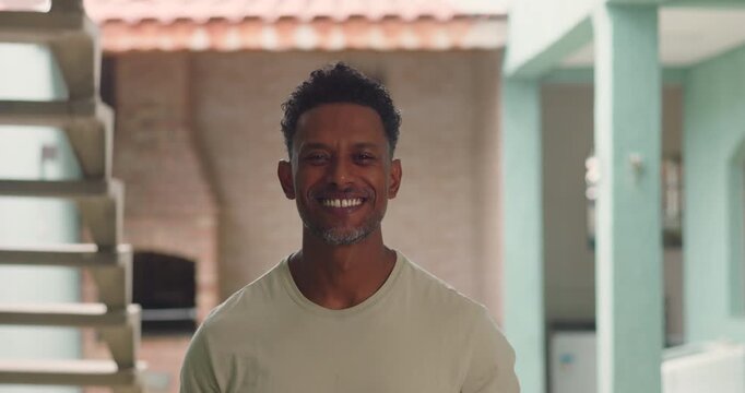 Man smiling warmly standing indoors in modern home with staircase and exposed brick wall in background relaxed and confident posture African descent individual