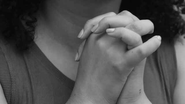 Close-up of woman in monochromatic scene with hands clasped in prayer, looking up with joyful expression, radiating hope, faith, spirituality, gratitude, and inner peace