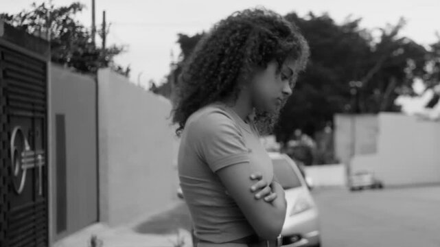 Teenage girl standing in monochromatic scene with arms crossed, distant expression, looking away, conveying sadness, reflection, contemplation, and emotional solitude