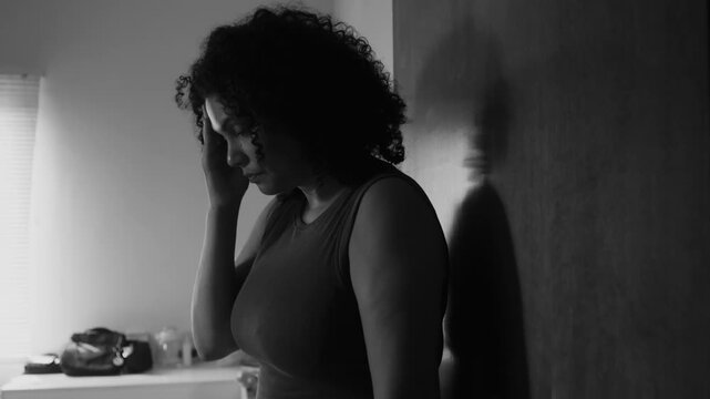 Woman leaning against wall in monochromatic scene, holding head with hand, expressing stress, anxiety, deep thoughts, and emotional turmoil in contemplative moment