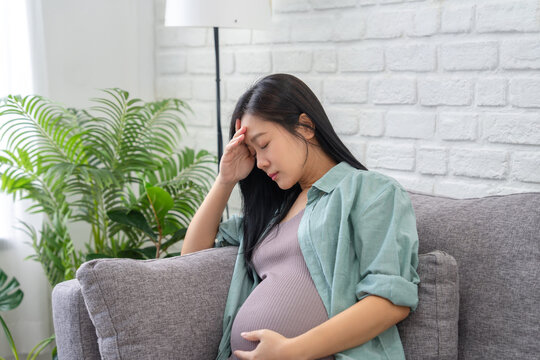 Asian pregnant woman experienced depression during her pregnancy &ndash; she had headaches and stomach pains while sitting on the sofa in the living room at home.