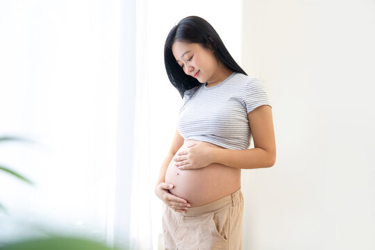 Beautiful pregnant Asian woman hugging her belly, enjoying her pregnancy