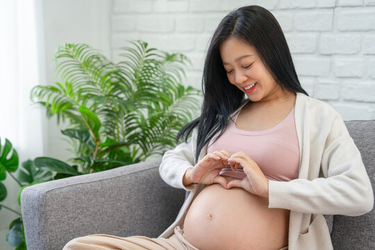 Asian pregnant woman holds her hand on her belly, touching her baby and caring about her health.