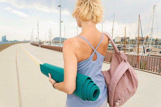 Walking by the Marina With a Yoga Mat and a Backpack