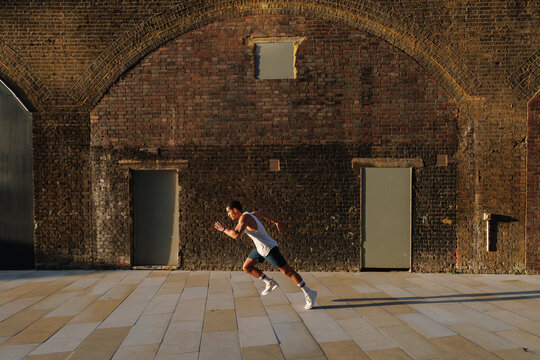 Young man sprinting against brick wall architecture