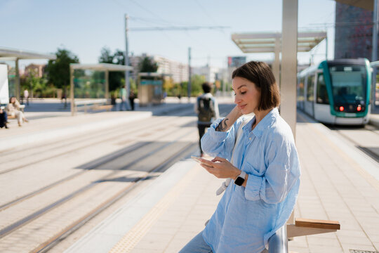 Woman texting on her phone and waiting for the tram at the station