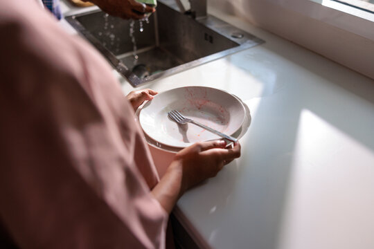 A person holding a dirty plate near kitchen sink