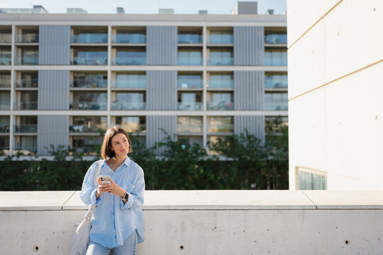 Woman Leaning Against Wall Using Smartphone in Modern District