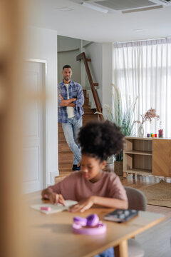 A father watches his daughter study at home.