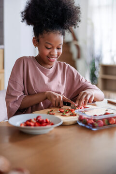 Smiling girl chopping fresh strawberries at home
