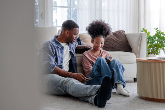 Father and daughter bond while using smartphones at home.