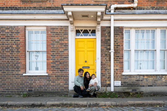 Family Sitting Outside Traditional London House With Yellow Door
