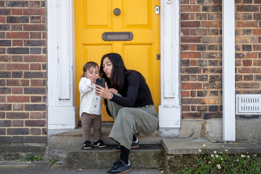 Mother Using Smartphone With Baby Outside London Door