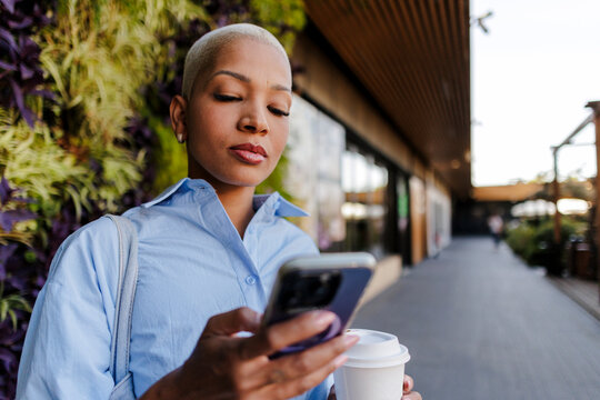 Woman checking smartphone while walking and drinking coffee