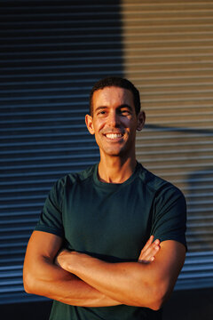 Young man smiling with crossed arms outdoors