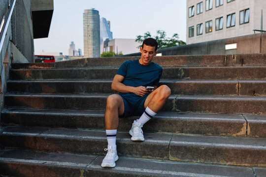 Young man resting on stairs checking mobile phone