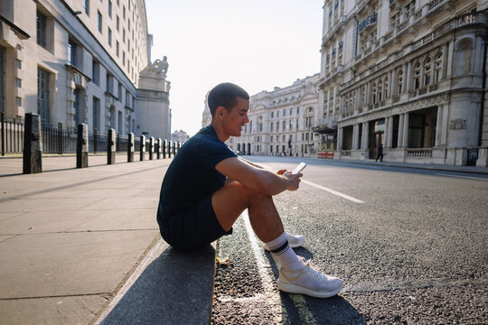 Young man taking a break checking phone on city street