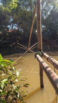 Traditional bamboo fishing trap structure installed over a calm muddy river in rural nature