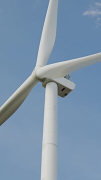 Wind turbine rotating blades generating renewable energy against blue sky with white clouds. Alternative green power source