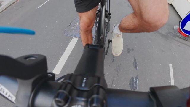 A man is riding a bicycle in a POV angle thats shows his feet in London, UK on a sunny day. Traffic is low and not busy