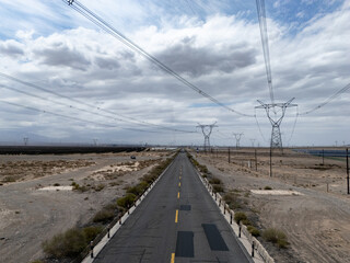 Fototapeta premium Desert highway stretching towards distant power transmission towers under cloudy sky