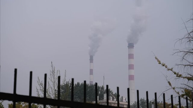 Thick White Smoke Billowing from Tall Industrial Chimneys Behind a Fence