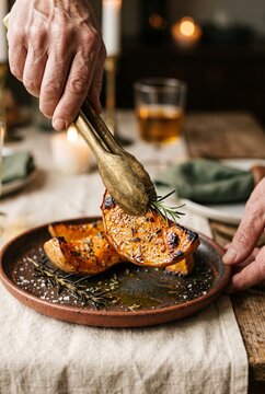 Person Serving Roasted Butternut Squash with Metal Tongs at a Thanksgiving or Autumn Dinner Table