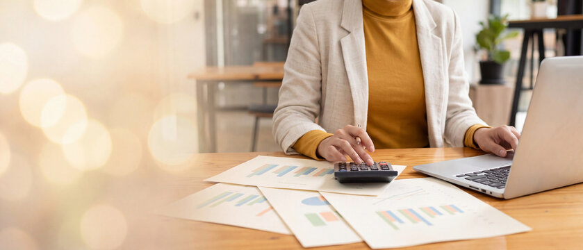 Accountant using calculator with printed financial charts and graphs on desk, analyzing budget data. Concept of accounting, financial planning and business analytics report.