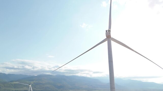 Close up of a large wind turbine with its massive blades turning against a bright sun and blue sky, producing clean, sustainable, and renewable energy to fight climate change