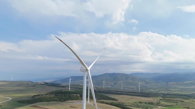 Close up aerial view of a wind turbine spinning its large blades, harnessing clean, renewable energy with other windmills in the background on a sunny day