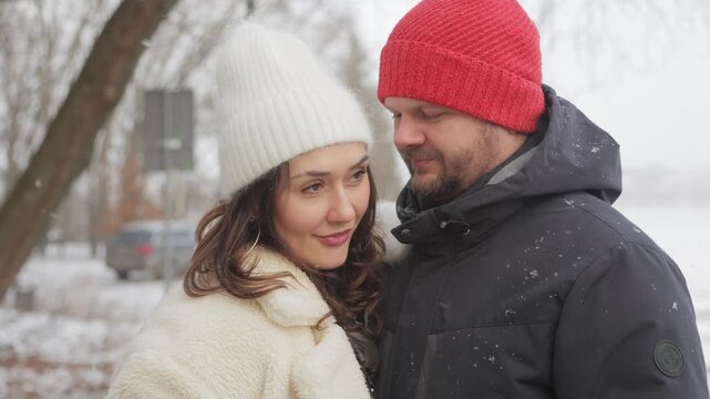 Romantic couple embracing and smiling during winter snowfall