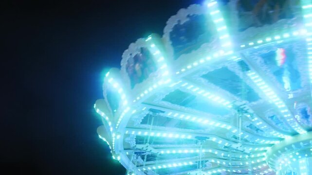 Abstract view of a glowing swing ride spinning with bright neon lights at a night amusement park.