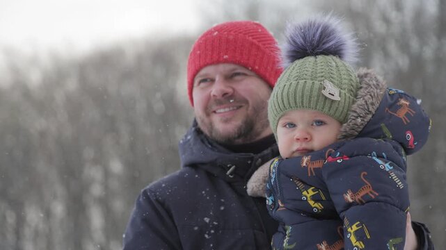 Happy father holding his baby son enjoying the first snow