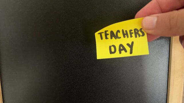 Hand placing Teachers Day sticky note on blackboard