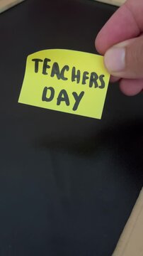 Hand holding teachers day sticky note on black background