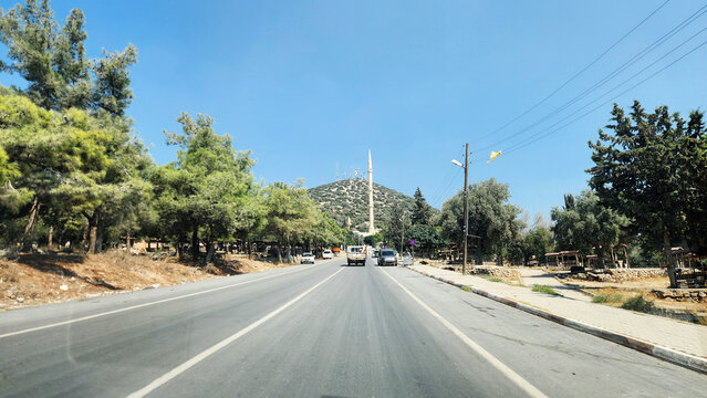 The road leads to the historic Ashab-ı Kehf Cave near Tarsus, a sacred site associated with the Seven Sleepers. Framed by Mediterranean vegetation, Enculus Mountain