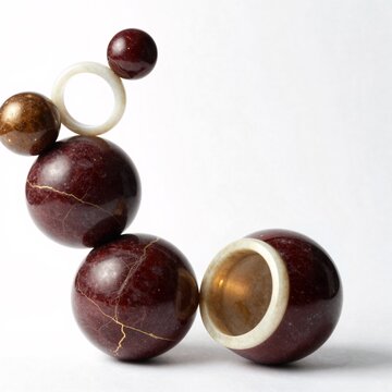 group five spheres arranged horizontal line white background spheres different sizes shapes largest one center two smaller ones either side largest sphere dark red color cracked texture while smaller